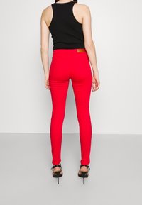 Jeans skinny rojos con una textura suave, que cuentan con un parche en la parte trasera y bolsillos traseros. Llevados con una camiseta sin mangas negra y sandalias de tacón alto.