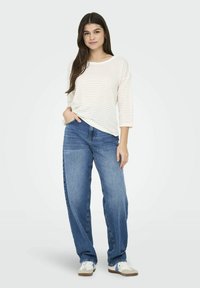 Witte gestreepte lange mouwen shirt over blauwe loszittende jeans, gecombineerd met witte sneakers met grijze en marineblauwe accenten.