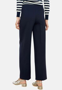 Laiad säärega tumelillad püksid, valmistatud siledast kangast. Omavad hästiistuvat lõiget kõrge vöökohaga ja peente voltidega, kombineeritud hõbedaste jalatsitega.