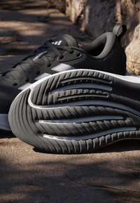 Paire de chaussures de sport noir et blanc sur un chemin en terre, avec une chaussure montrant un motif de semelle détaillé.