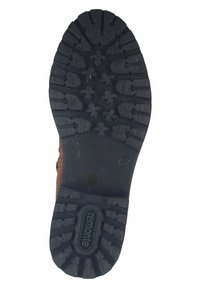 Semelle de chaussure en caoutchouc noir avec des motifs de crampons profonds, comportant un logo central et divers designs de grip pour une meilleure traction.