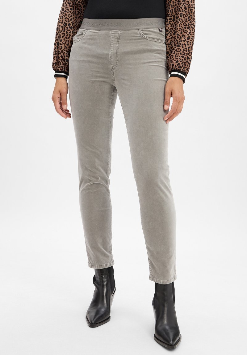 Pantalon gris clair slim-fit avec taille élastique, porté avec des bottines noires pointues et un haut à manches longues imprimé léopard.