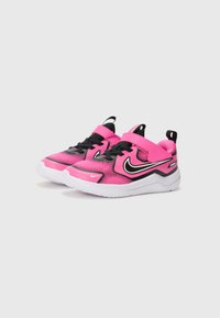 Baskets de sport roses et noires avec une tige en maille, semelle en caoutchouc et fermeture Velcro. Présentent un swoosh Nike blanc sur le côté.