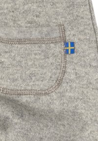 Grå tygtröja med en framficka, avslutad med ljusbrun sömnad. En liten blå och gul etikett är synlig i hörnet.