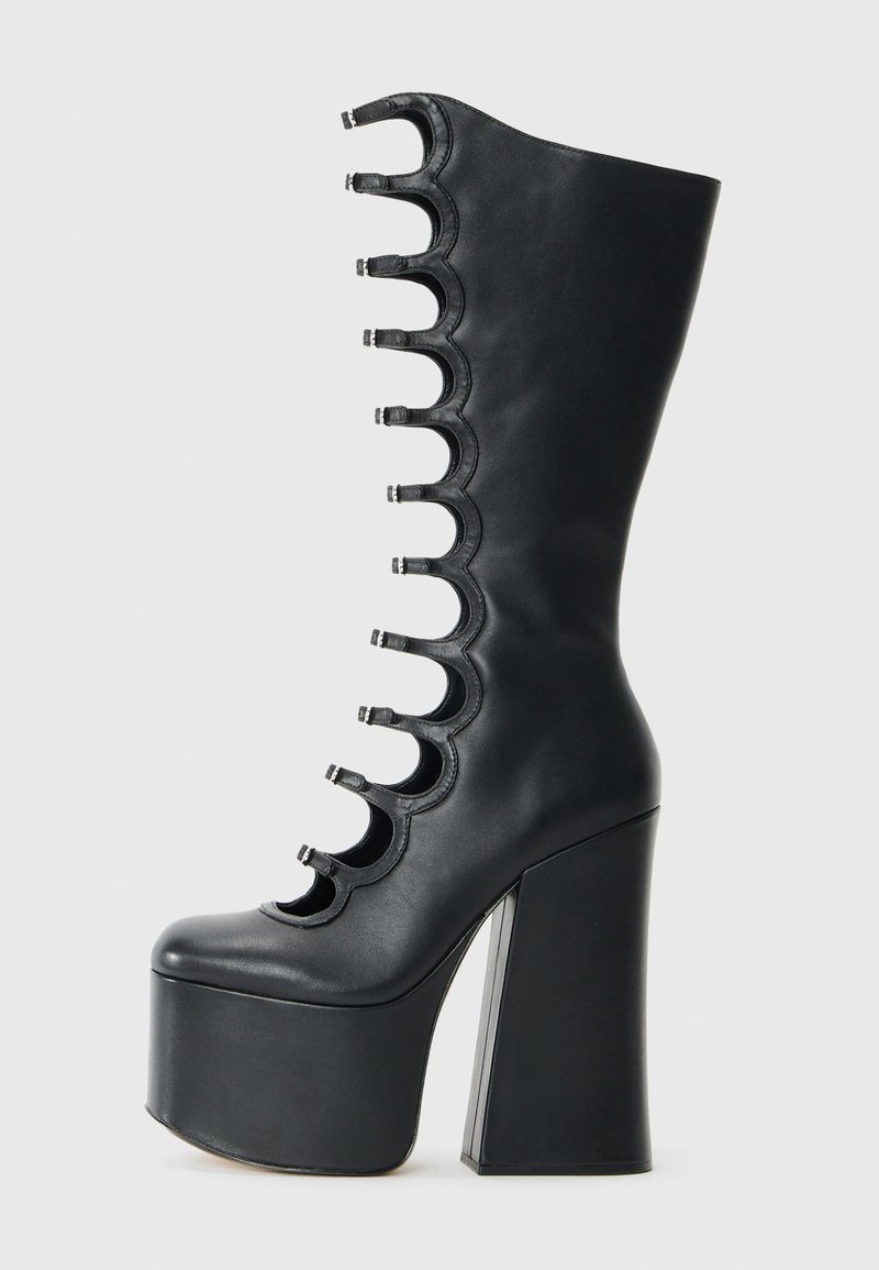 Botte en cuir noir à plateforme avec un haut talon épais et un avant découpé à bords festonnés comportant huit petites lanières à boucle.