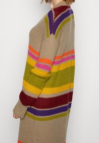 Stickad kavaj i beige med horisontella ränder i violett, grönt, gult, rosa och rött. Har en avslappnad passform och ribbade ärmslut.