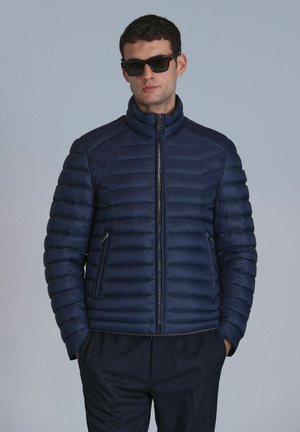Navy puffer jacket with horizontal quilted design, zip closure, and high collar. Features two side pockets and a smooth, shiny texture.