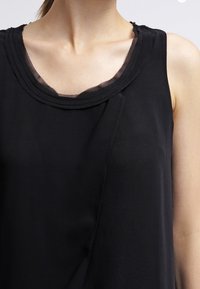 Top nero senza maniche con scollo rotondo, caratterizzato da un bordo testurizzato e un tessuto liscio. Design semplice con dettagli di cucitura discreti.