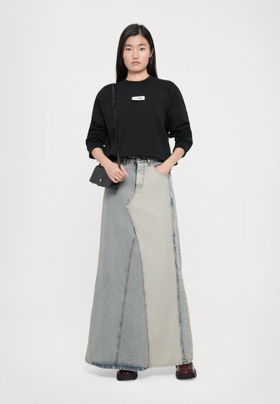 Oversized black sweatshirt with logo, paired with a long, two-tone denim skirt featuring a unique cut and seam details. Small black handbag.