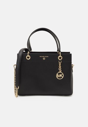 Sac à main en cuir noir de Michael Kors avec deux poignées, bandoulière en chaîne dorée et pendentif logo doré sur fond blanc uni.