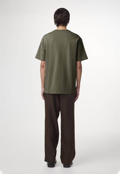 Olivenfarvet kortærmet T-shirt lavet af bomuld, vist med løse brune bukser. Simpelt design, rund halsudskæring, ingen synlige mønstre.