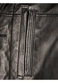 Detail einer schwarzen Lederjacke mit einer vertikalen Reißverschlusstasche, gesteppten Akzenten und glatter Textur. Nahaufnahme des Stoffes und Designs.