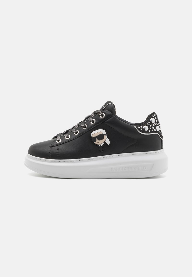 Black leather sneakers with white platform sole, featuring gray laces and a cartoon logo on the side. Decorative accents on the heel.