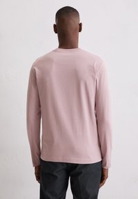 Długi rękaw koszula w miękkim różowym jerseyu z okrągłym dekoltem i prostym krojem, zestawiona z ciemnymi spodniami, widziana z tyłu.