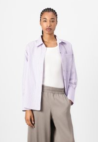 Light purple striped button-up shirt with a single chest pocket, worn over a white tank top, paired with light gray elastic waist pants.