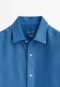 Lingenskjorta i solid blå färg, med spridd krage, framknäppning med vita knappar och en slät textur. Varumärkesetikett synlig.