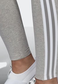 Leggings grigi realizzati in un materiale morbido e elastico, con tre strisce bianche orizzontali lungo il lato esterno. Abbinati a scarpe bianche.