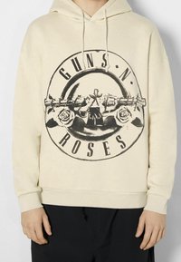 Sudadera crema con un gran diseño gráfico negro que incluye el texto "GUNS N' ROSES" y rosas, con capucha ajustable y puños acanalados.