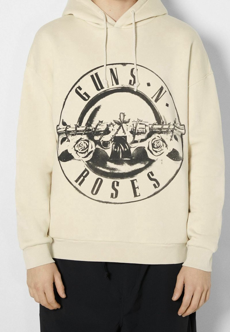 Sudadera crema con un gran diseño gráfico negro que incluye el texto "GUNS N' ROSES" y rosas, con capucha ajustable y puños acanalados.