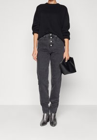 Černý oversized svetr a černé džíny s vysokým pasem a zapínáním na knoflíky. V kombinaci s černými koženými kotníkovými botami na podpatku a malou kabelkou.