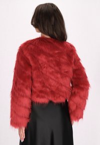 Giacca corta in finta pelliccia rossa con una morbida texture pelosa e maniche lunghe. Il design presenta un colletto rotondo e un orlo leggermente irregolare.