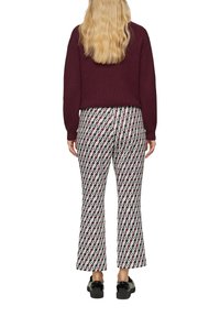 Pull à côtes bordeaux associé à un pantalon large à motifs présentant des designs géométriques dans des tons rouges, blancs et verts. Chaussures noires.