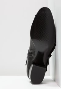 Botte en cuir noir à finition lisse, avec une fermeture éclair latérale et une semelle en caoutchouc plate présentant des rainures horizontales pour l'adhérence.