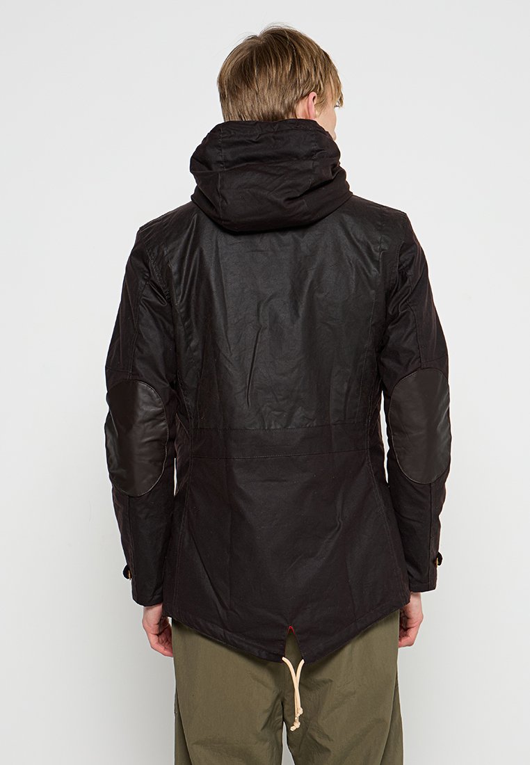 Black outdoor jacket with a hood, brown elbow patches, long back hem, and drawstring detailing at the waist. Textured fabric finish.