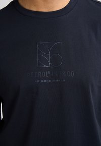 T-shirt in cotone blu navy con colletto a giro, caratterizzata da un design del logo minimalista in azzurro e la scritta "PETROL IND&CO NORTHWOOD WISCONSIN USA."