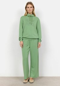 Grön huva med texten "FEMME and FIERCE", tillsammans med matchande löst sittande byxor. Mjuk tyg, avslappnad design och enkla accenter.
