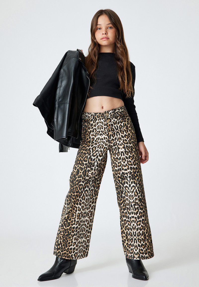 Pantalones de pierna ancha con estampado de leopardo en tejido beige, marrón y negro. Combinados con un top negro corto y una chaqueta de cuero, complementados con botas negras.