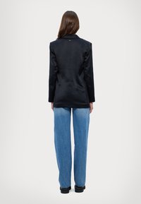 Blazer in satin nero con uno spacco singolo e revers a punta, abbinato a jeans ampi azzurri e scarpe nere robuste.