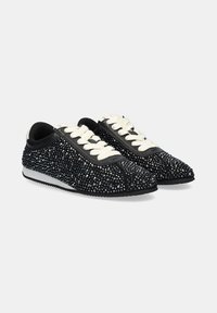 Zapatillas negras cubiertas de pequeñas y brillantes piedras de strass. Los cordones son blancos y la suela texturizada es negra, completando el diseño. Silueta de corte bajo.