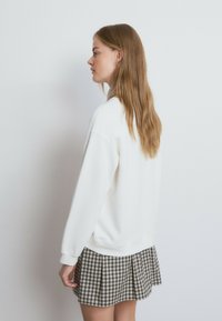 Sudadera blanca de mangas largas y cuello redondeado, combinada con una falda de cuadros con pliegues. El cabello es largo y liso, con una textura natural.