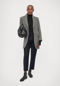 Abrigo gris de espiga, suéter negro de cuello alto, pantalones navy ajustados, bolso negro y calcetines cortos grises combinados con zapatos negros.