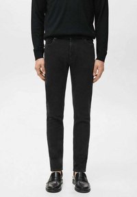 Jeans ajustados negros con una textura suave, con una pretina estándar y detalles sutiles de costura, combinados con mocasines negros.