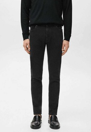 Jeans ajustados negros con una textura suave, con una pretina estándar y detalles sutiles de costura, combinados con mocasines negros.