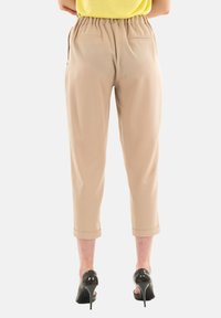 Pantaloni beige a vita alta con elastico, tasche laterali e risvolti, abbinati a scarpe con tacco nere.