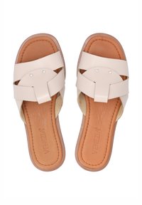 Lichtbeige slide sandalen met twee overlappende banden, zilveren studs en een bruine gewatteerde binnenzool. Glad leer en zachte textuur.