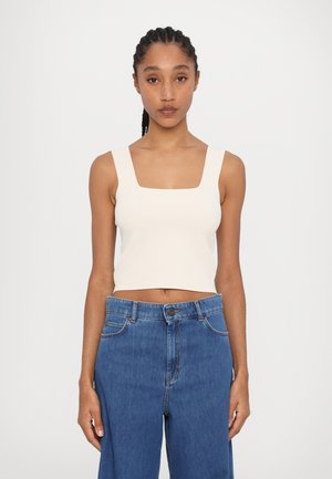 Kremfarget kort tanktopp med firkantet utringning, kombinert med høyhåndte blå denimjeans med avslappet passform og standard sømmer.