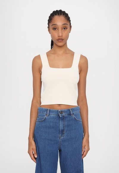 Top cropped de couleur crème avec un décolleté carré, associé à un jean en denim bleu taille haute avec une coupe décontractée et des coutures standard.
