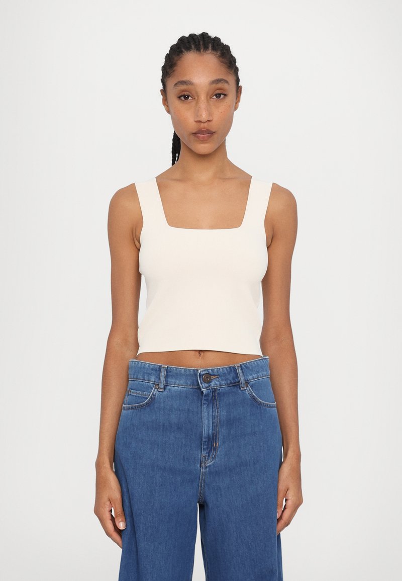 Cream-colored cropped tank top with a square neckline, paired with high-waisted blue denim jeans featuring a relaxed fit and standard stitching.