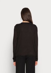 Suéter negro de manga larga con cuello redondo, puños acanalados y corte relajado. Textura suave y aberturas laterales en el dobladillo.