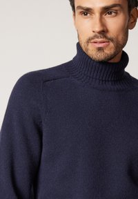 Mörkblå polotröja i mjukt stickat material. Har en ribbad halsringning och slät yta, med raglanärmar.