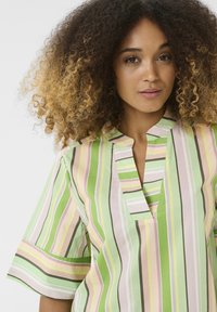 Lühikeste varrukatega topp, millel on vertikaalsed triibud rohelises, roosas ja valges. Sellel on V-kujuline kaelus ja see on lõdva lõikega, valmistatud kergest kangast.