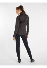 Giacca nera aderente con colletto alto, maniche lunghe e tessuto testurizzato. Abbinata a pantaloni scuri slim-fit e scarpe nere eleganti.
