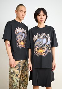 Black graphic t-shirts with a detailed scorpion design. One person wears camouflage pants, the other a black pleated skirt.