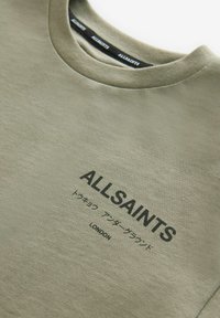 Alieji žalia medvilninė marškinėlių su apvaliu iškirpimu, su juodu spausdintu tekstu: "ALLSAINTS" ir papildomais japonų simboliais, lygus paviršius.
