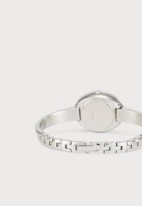 Montre-bracelet en argent avec un boîtier rond, un bracelet à maillons en métal et une finition polie. Le dos présente une surface lisse avec un minimalisme dans l'ornementation.