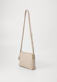 Beige křížová taška s texturovaným koženým povrchem, obdélníkový tvar a zipovým uzávěrem. Obsahuje nastavitelný popruh a detail v podobě střapce.